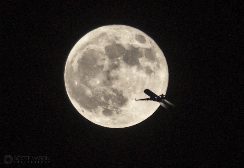 a silhouetted plane flying in front of the full moon