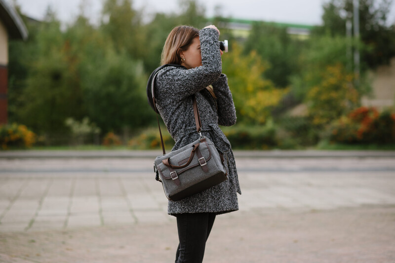 A woman carrying a grey messenger bag and using a camera