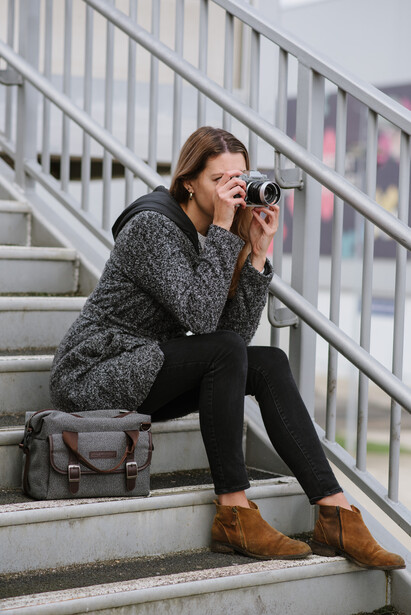 A woman sat on steps with a bag and camera in hand
