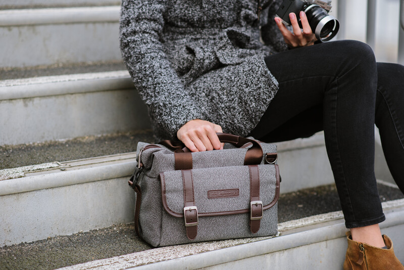 A woman sat on steps with a grey bag next to her and a camera in hand