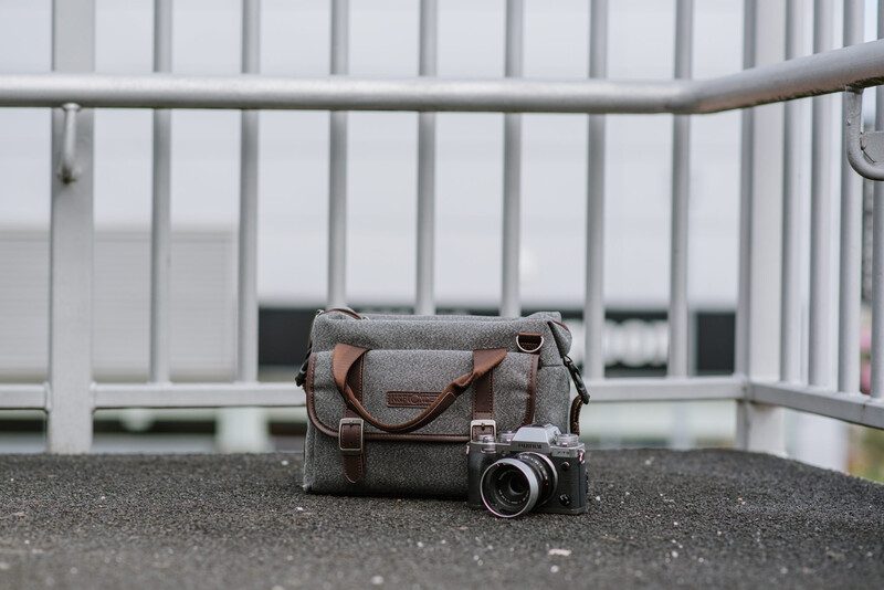 A grey messenger bag and a camera on pavement