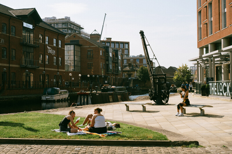 Several people enjoying sun shine by a canal.