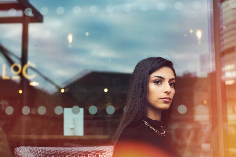 A portrait of a dark haired woman sat outside at a table.