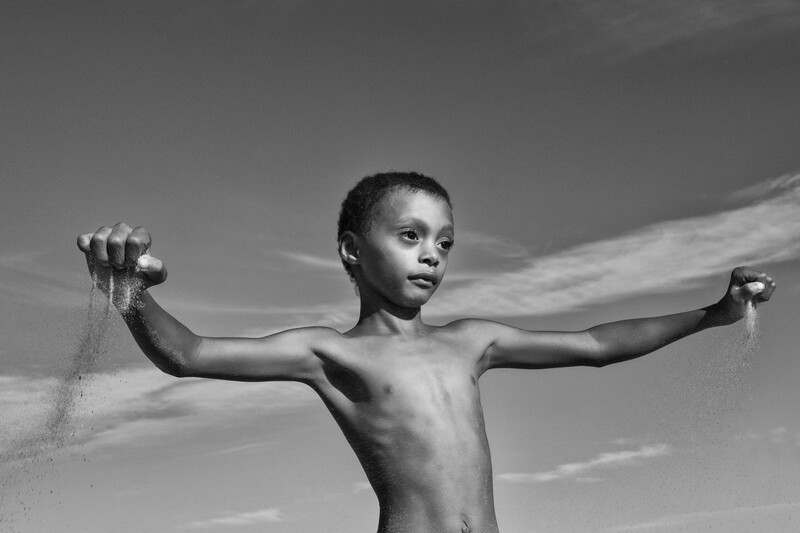 A young boy holding sand in his hands.