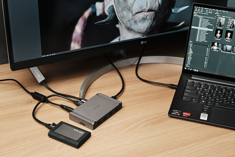 External hard drives and portable SSD connected to laptop and monitor displaying video editing software.