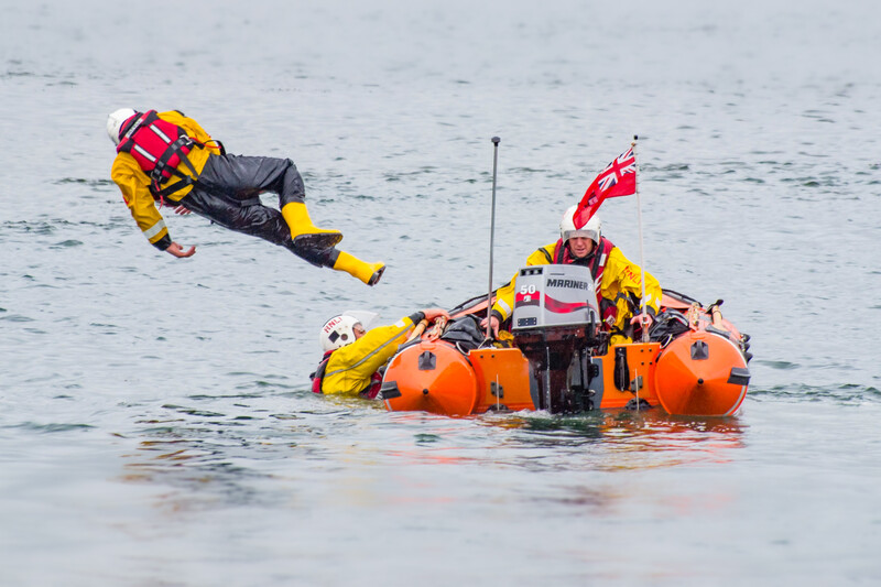 Rescue team members in yellow and red gear conducting water rescue training with orange inflatable equipment in shallow water.