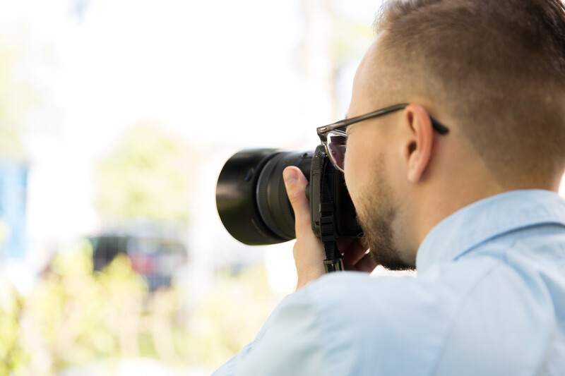 Photographer wearing glasses holding camera to his eye while shooting outdoors.