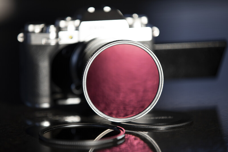 Deep magenta circular camera filter positioned in front of blurred film camera body.