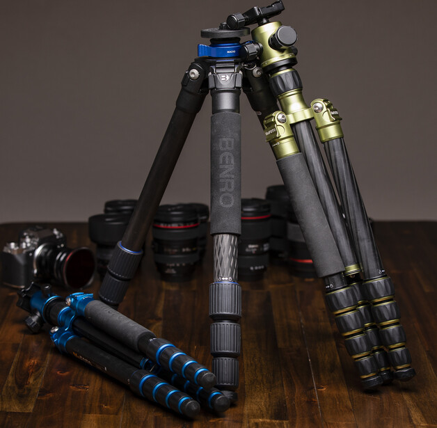Collection of professional tripods and monopods with blue and gold accents arranged on a wooden surface.