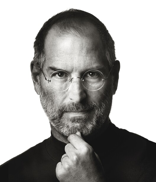 Man with beard and glasses in contemplative pose with hand near face against white background.