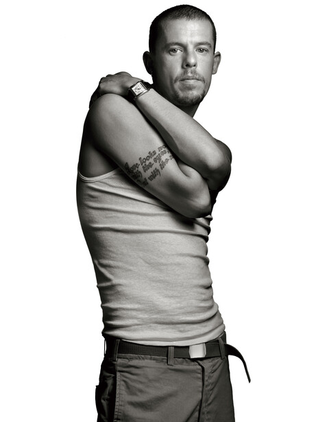 Man in light-colored tank top posing with arms crossed over chest against white background.