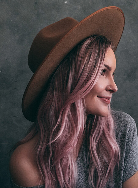 Woman with long pink hair wearing a brown cowboy hat, photographed in profile against a textured gray background.