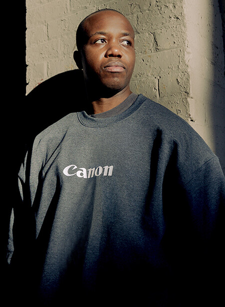 Man wearing Canon branded t-shirt against textured wall with dramatic side lighting.