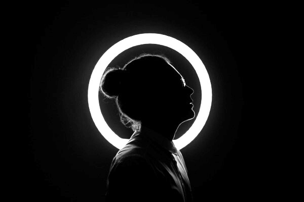Silhouetted profile of a person backlit by a glowing circular light ring against a dark background.