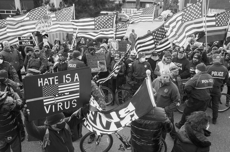 Black and white photograph of a crowded street protest with American flags and police presence.