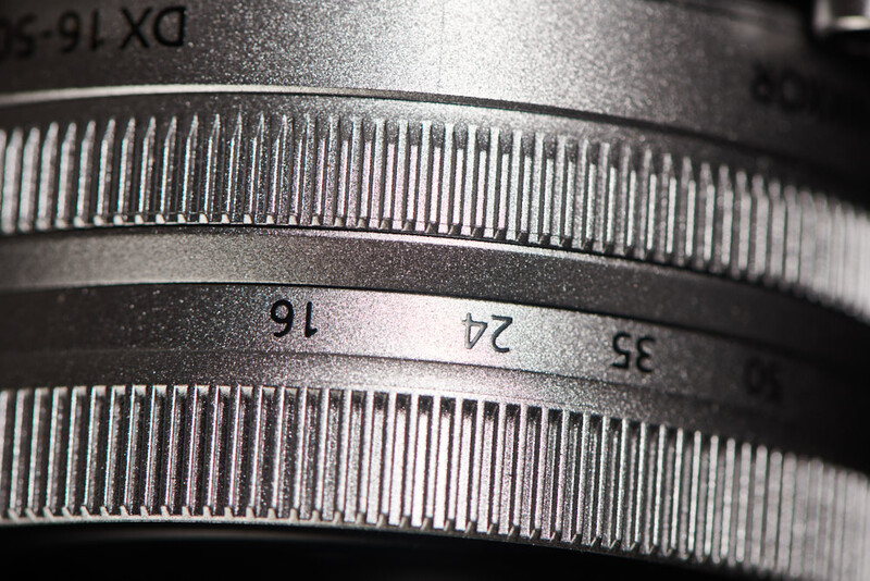 Close-up of camera lens focus ring with depth-of-field markings and distance scale engraved on metal barrel.