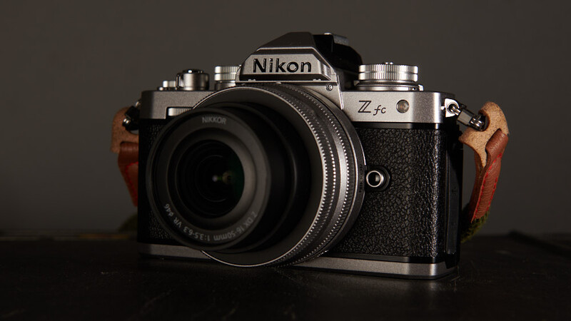 Nikon Zfc mirrorless camera with silver top plate, black body, and wood grip panels against dark background.