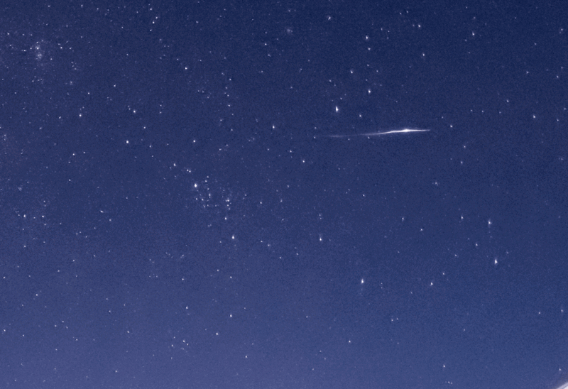 Deep blue night sky filled with stars and a bright meteor streaking across the upper right portion.