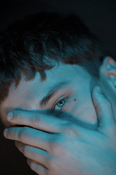 Person's face partially obscured by blue-tinted hands covering their eyes and mouth.