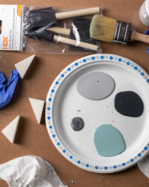 Painter's palette with three paint samples and brushes arranged on brown surface.
