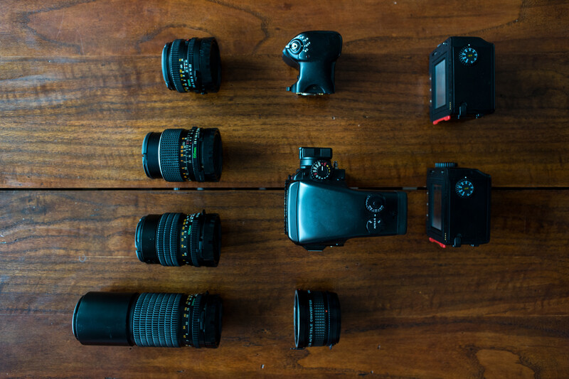 Camera body surrounded by various prime lenses arranged on a wooden surface.