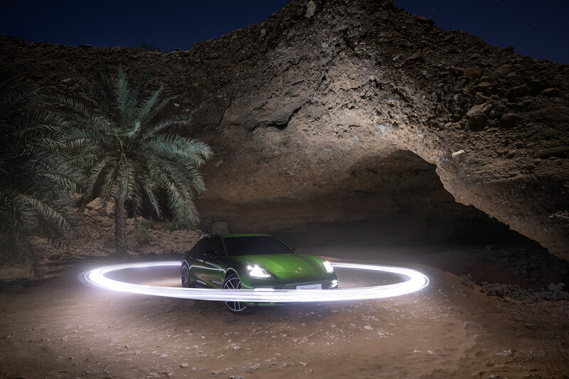 Green sports car surrounded by a bright LED light circle in a desert cave at night.