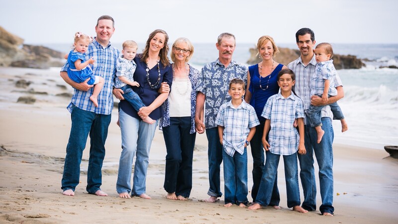 Multi-generational family group standing together on a sandy beach with ocean waves in the background.