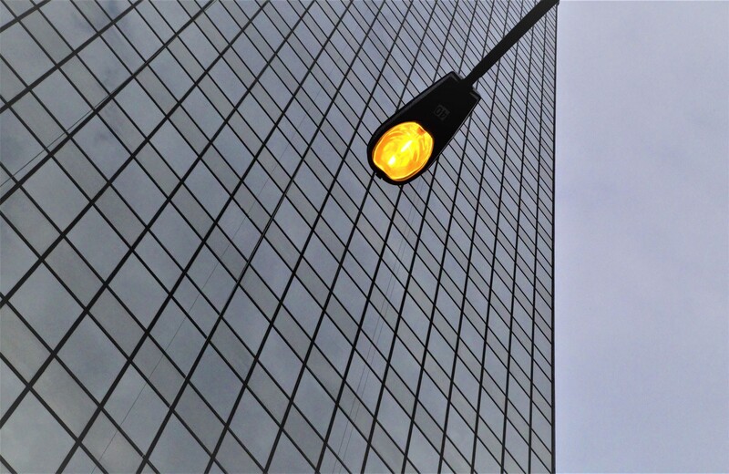 Yellow street light mounted on a cable against a modern glass and steel building facade.