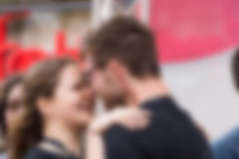 Two people in close conversation with blurred red and white background elements.