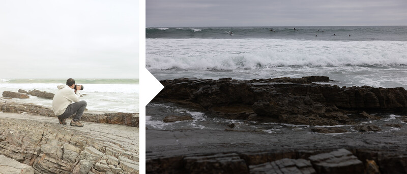 Photographer crouching on a driftwood log while shooting a coastal scene with waves and rocks.