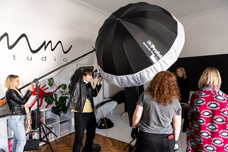 Studio photography session with large umbrella reflector and multiple people positioning equipment and talent.