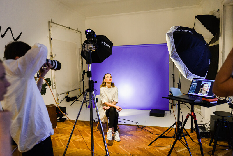 Professional studio portrait setup with subject seated against purple backdrop and three-light configuration.