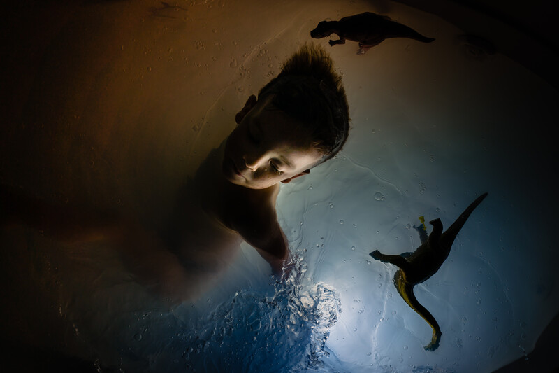 Underwater portrait of a person's face lit from below, with a diver silhouetted against the light source above.