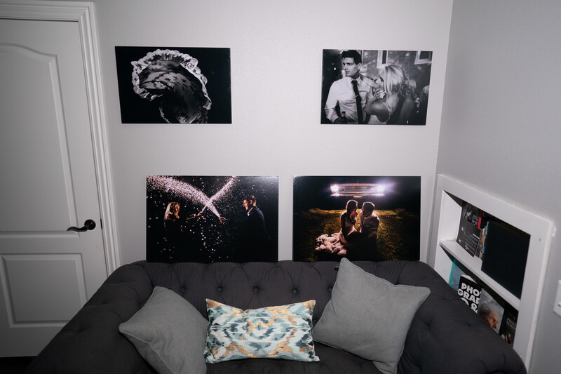 Black and white and color photographs printed large and mounted on white bedroom wall above dark sofa.