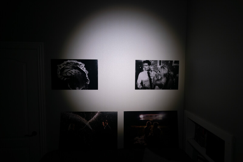 Four black and white photographs displayed on a gallery wall under spotlighting in a dark room.