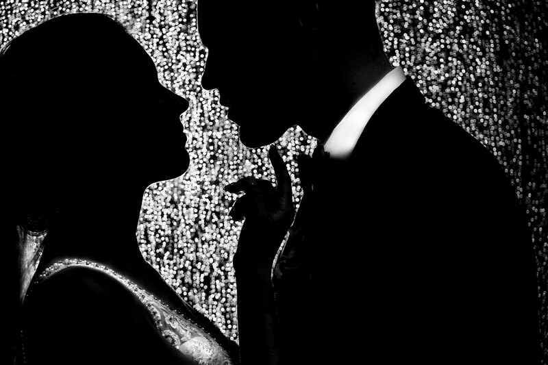 High-contrast black and white silhouette of two people about to kiss, with sparkling bokeh effect surrounding them.