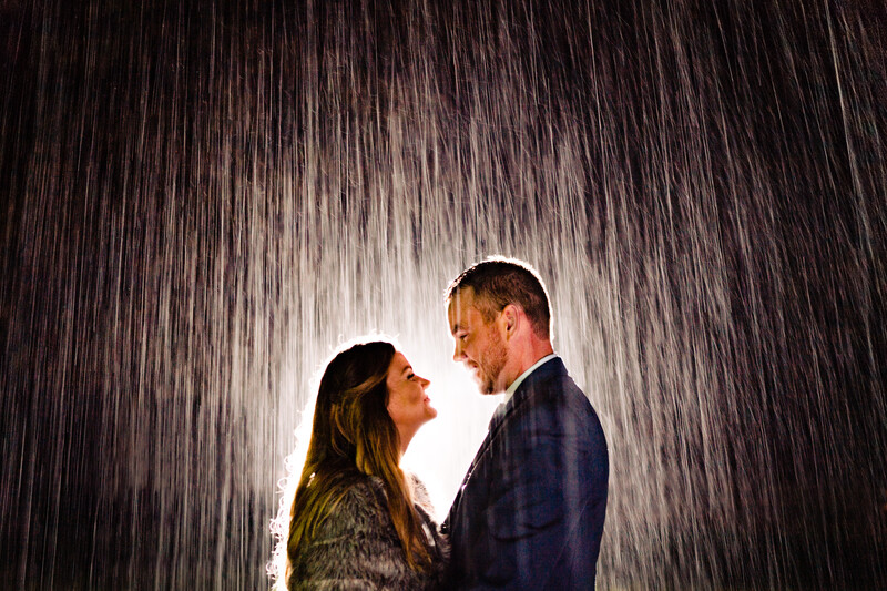 Couple facing each other in heavy rain with dramatic backlighting creating a luminous silhouette effect.