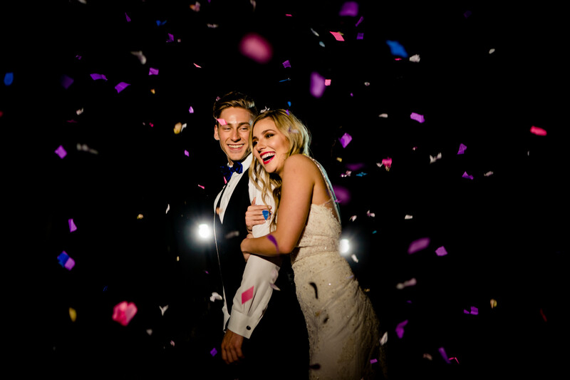 Couple in formal attire surrounded by colorful confetti at night.