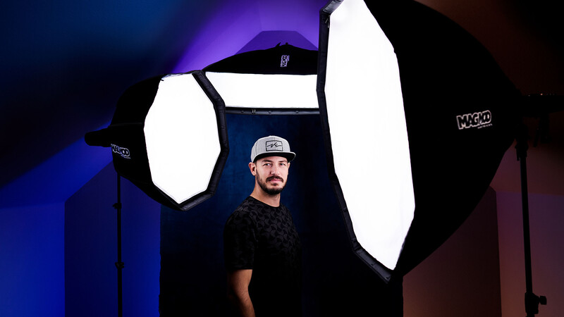 Photographer positioned between two large octagonal softboxes with blue and red gel lighting in the background.