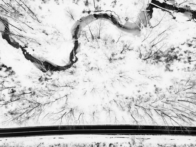 Aerial view of a snowy forest with a winding dark river cutting through snow-covered trees and terrain.