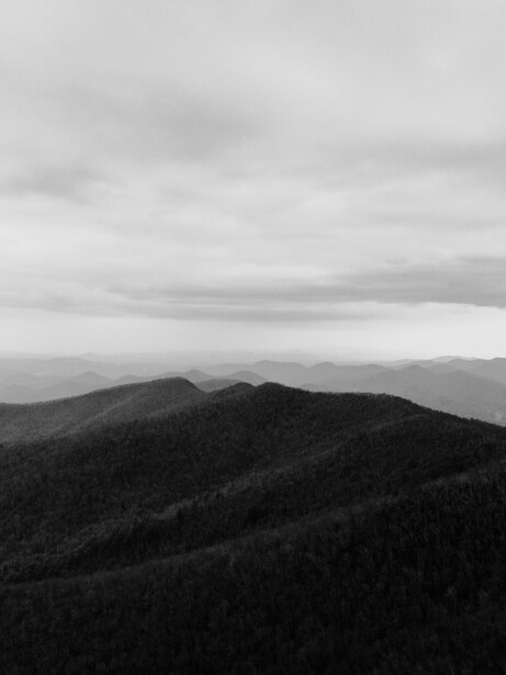 Forested mountain ridge with distant peaks beneath overcast sky.