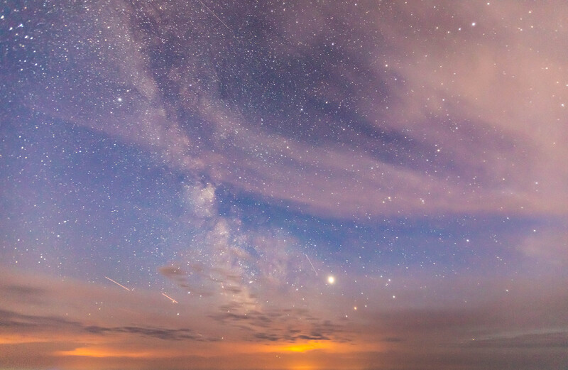 Milky Way galaxy stretching across twilight sky with golden sunset and scattered clouds.