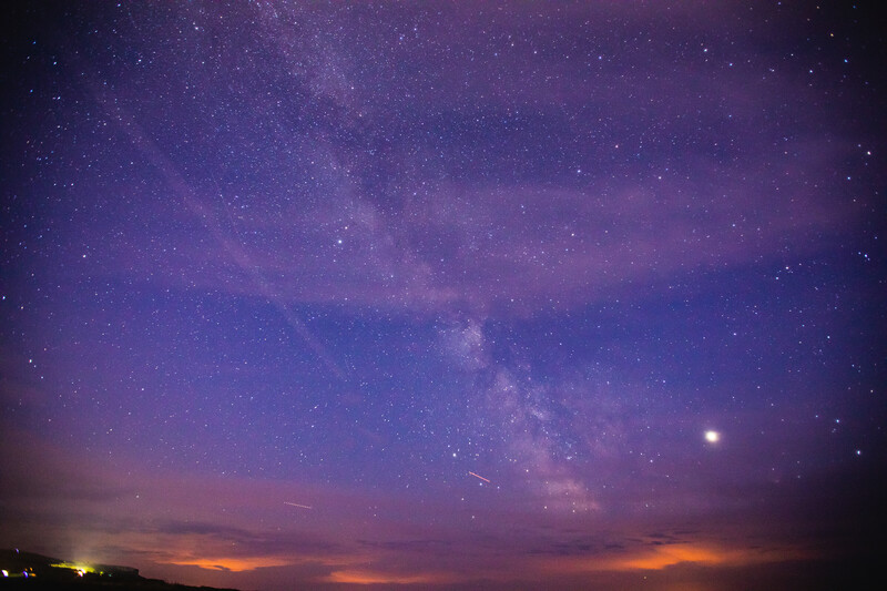 Milky Way galaxy stretching across twilight sky above orange and purple horizon at dusk.