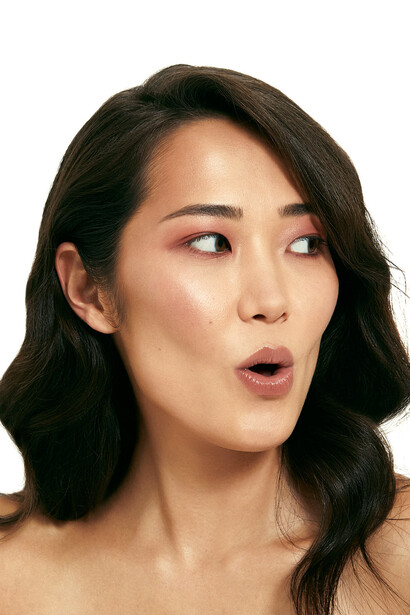 Woman with shoulder-length dark hair looking to the side with surprised expression against white background.