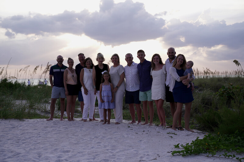 Large group of people standing together on a beach at dusk under dramatic cloudy sky.