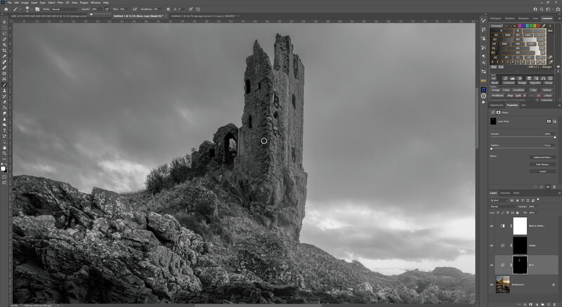 Black and white photograph of a ruined tower on a hillside with dramatic cloudy sky.