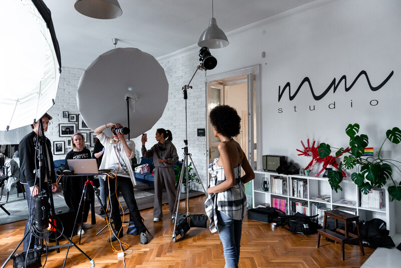 Professional photography studio session with multiple crew members operating lighting equipment and camera setup around a subject.