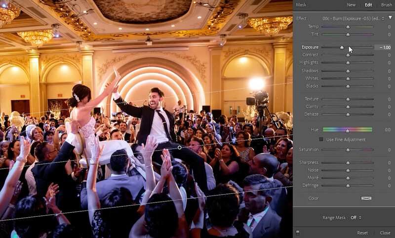 Wedding couple dancing on shoulders of guests in ornate ballroom with architectural arches and warm gold lighting.