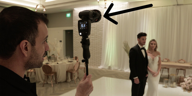 Photographer holding light meter pointed at bride and groom during indoor wedding reception.