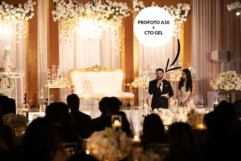 Bride and groom standing at ornate gold altar during wedding ceremony with white floral arrangements and warm ambient lighting.